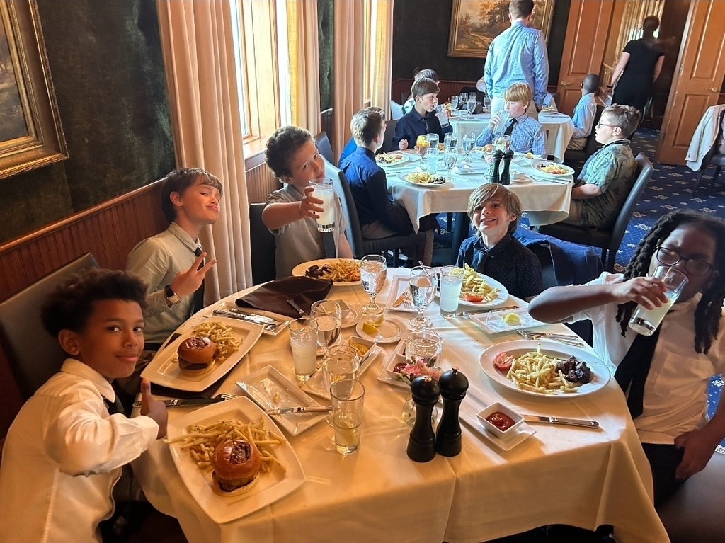A group of children seated around a table at a restaurant, all with plates of food in front of them.