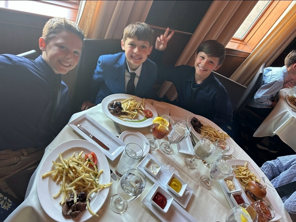 Three young boys seated at a table with a variety of food, including fries and sauces.