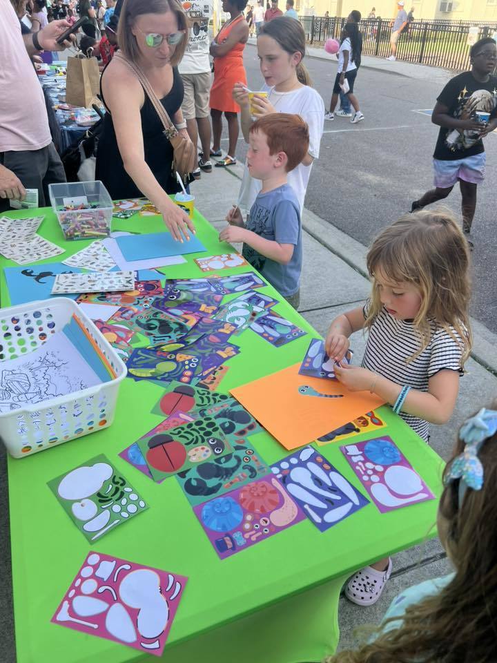 Children engage in a creative activity at a table with various colorful craft materials on a sidewalk.