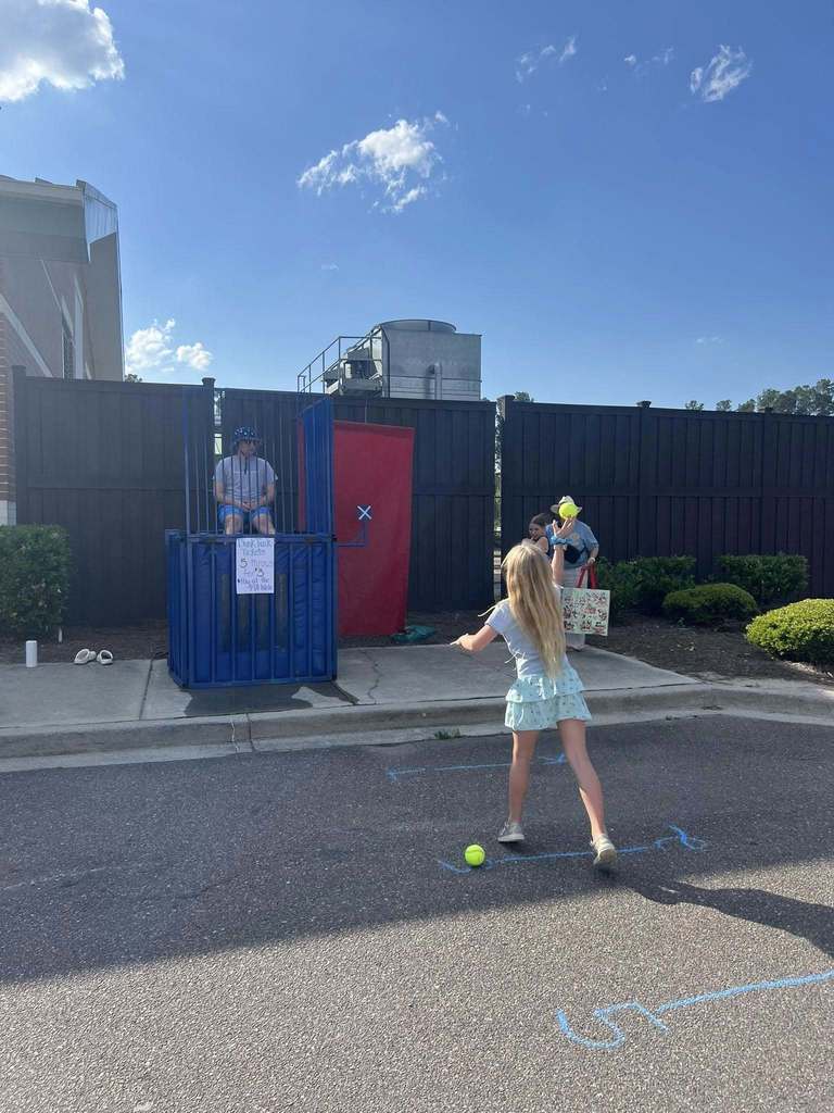 A girl throws a ball in a street with a black fence and red door behind her.