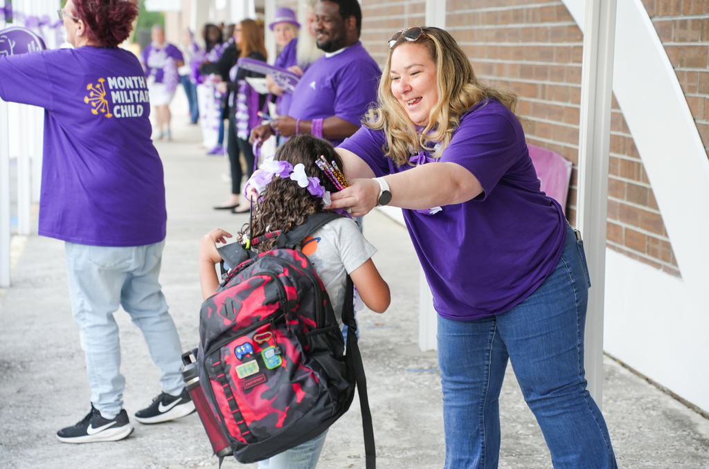 teacher putting a purple necklace on a student