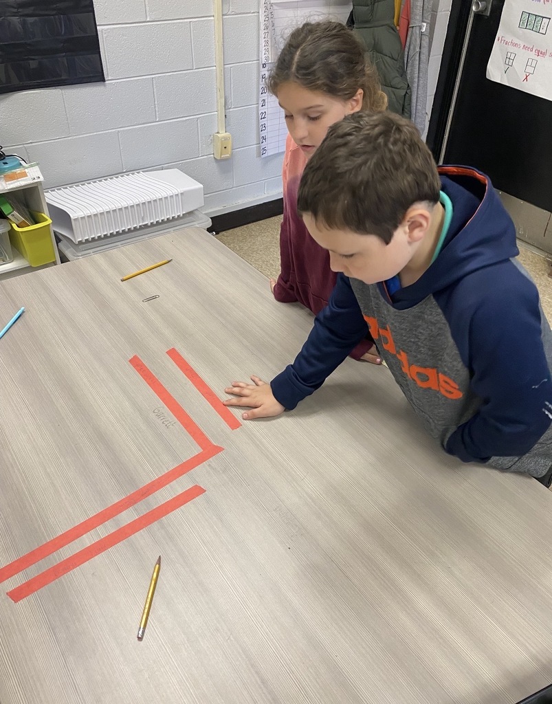 Two children working on a project with red tape on a table, one touching the tape.