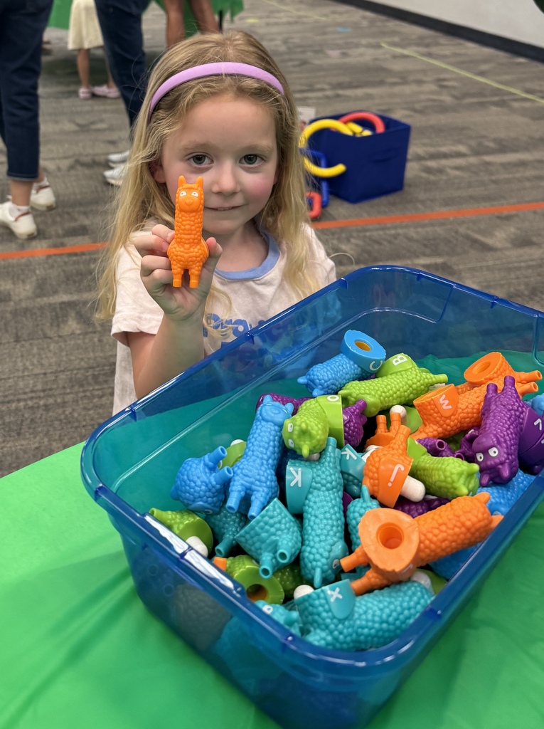 A young girl with a headband holds a toy animal from a large plastic bin full of colorful toys.