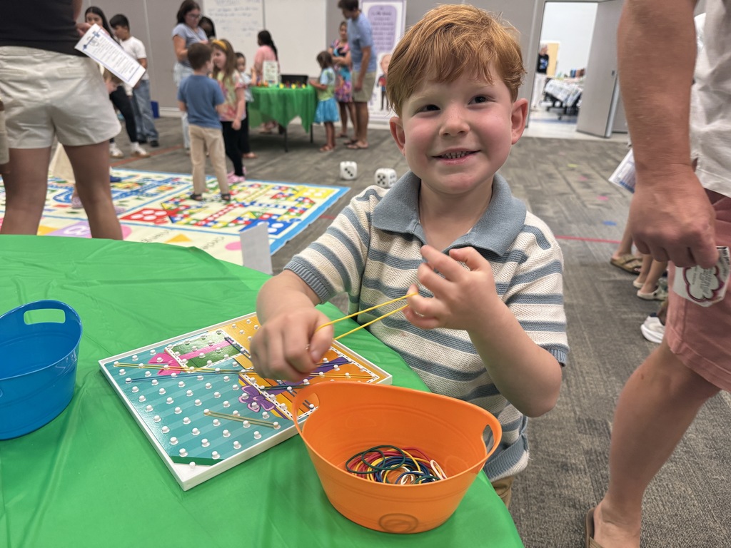 A young boy in a striped shirt sits at a table with a game, a bowl, and a map.