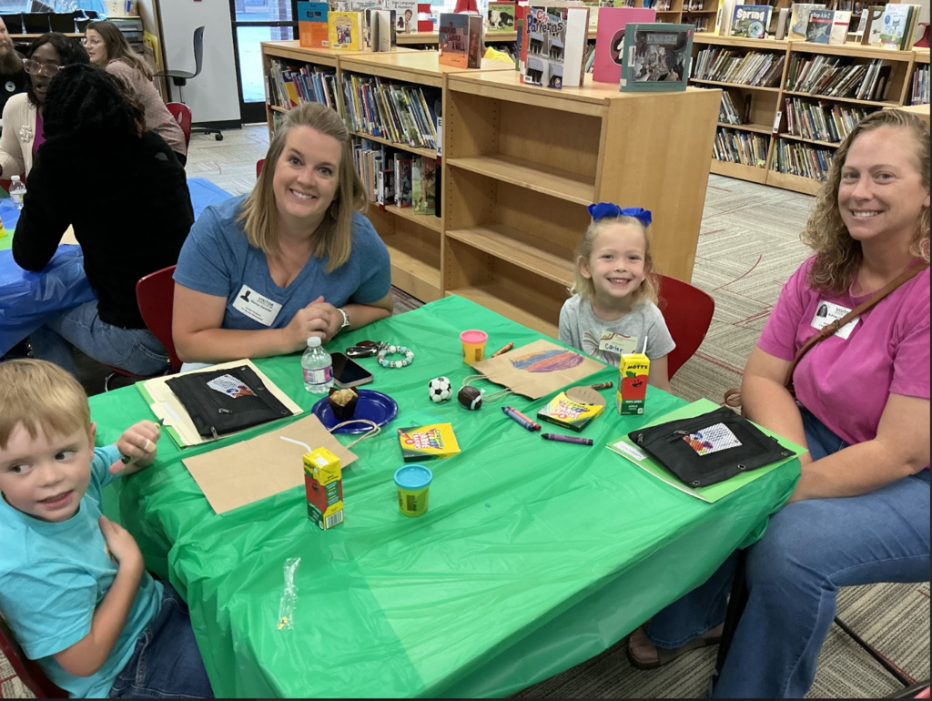 Family of four sitting at a green table with crayons and snacks laid out.