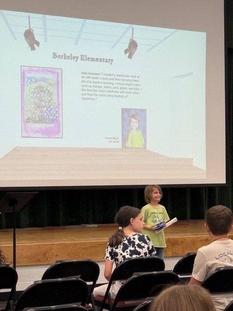 A projector screen displays a presentation while children sit in chairs. One child stands at the front.