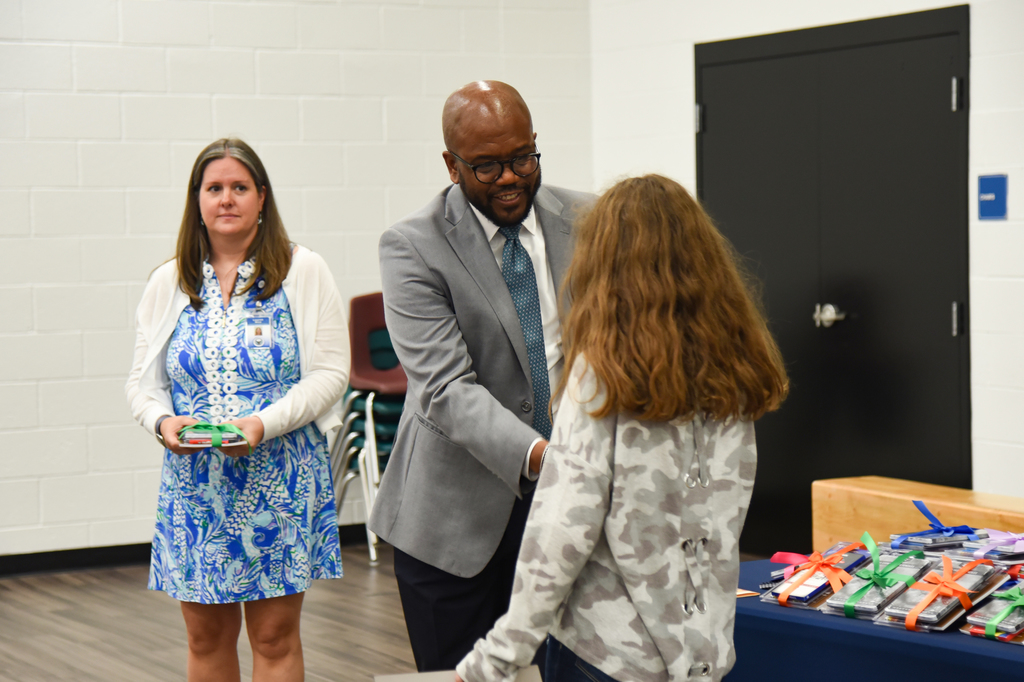 Three people stand in a room, Dr. Dixon shakes the hand of a student, and another woman stands nearby.