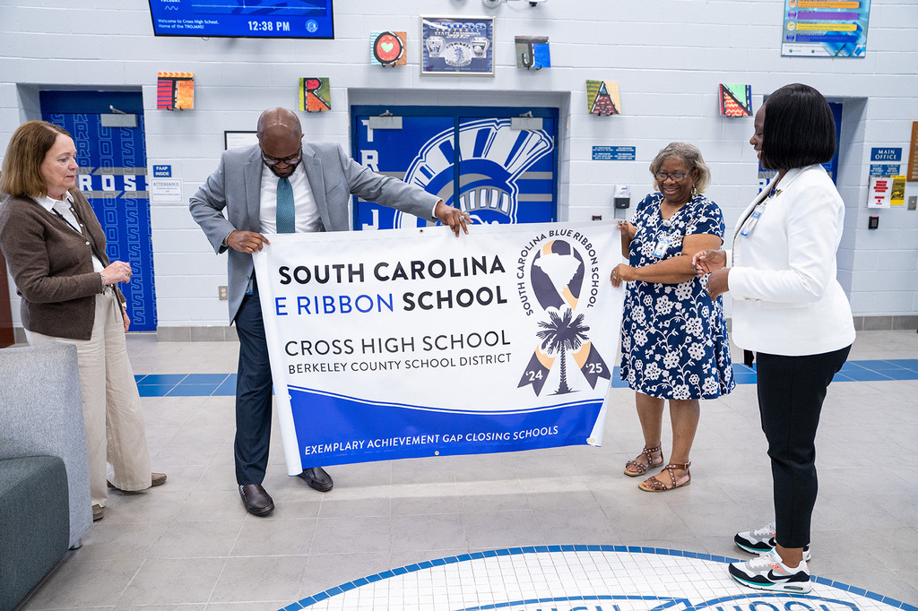 Four adults stand, holding a banner reading "South Carolina Blue Ribbon School" and "Cross High School". They are in a hallway with blue doors.