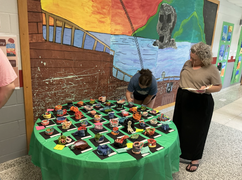 A woman and a person examine colorful art pieces on a table with a green cloth.