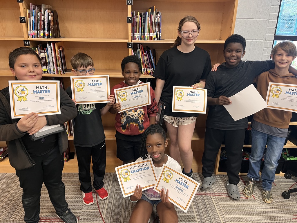 Group of students in a library with certificates in their hands, standing and crouching. Behind them are shelves filled with books.