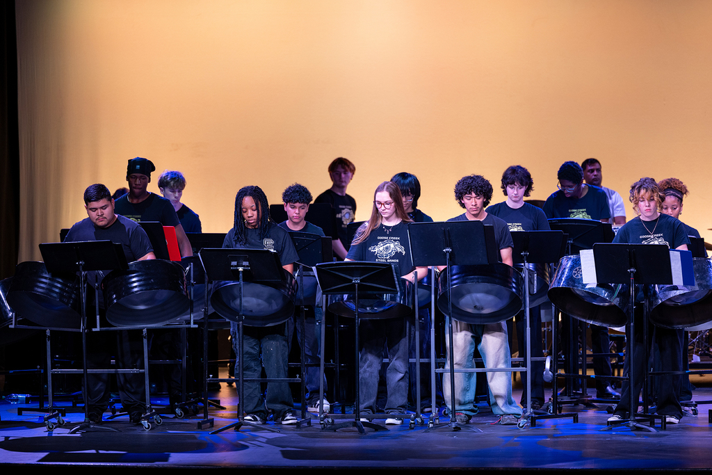 A group of people on stage playing steel drums with yellow background and blue lighting.