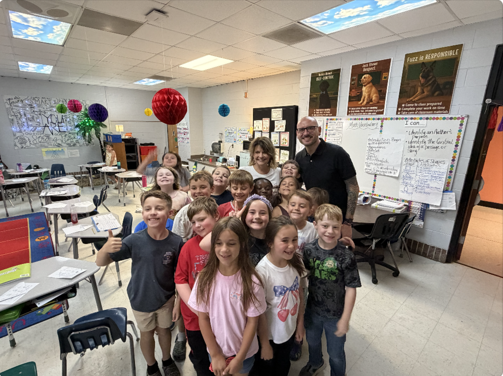 A classroom with a teacher and several students posing for a group photo.
