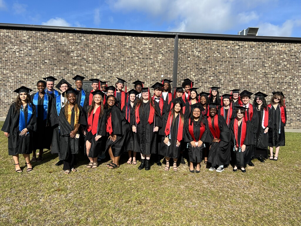 A group of people in black and red graduation gowns and hats pose for a photo.