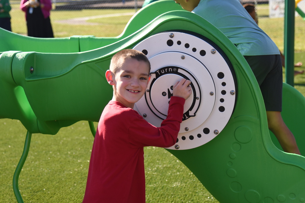 Child in a red shirt climbing a green slide at a playground, with others in background.
