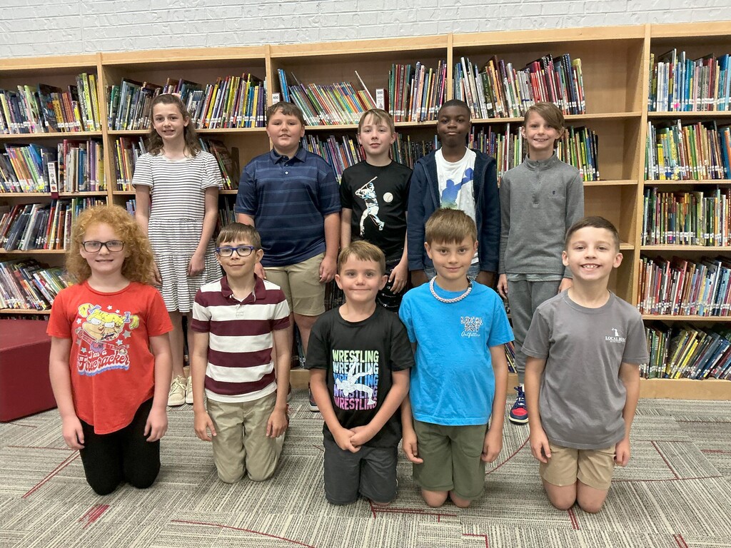 A group of kids in a library with rows of bookshelves in the background. They are all smiling.