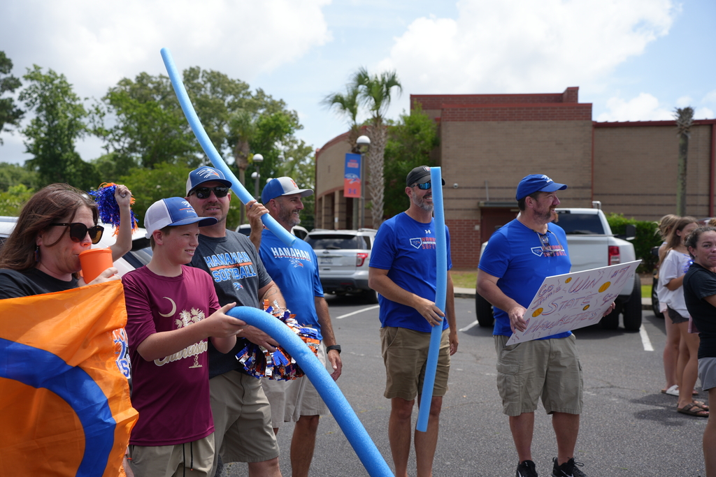 A group of people wearing blue shirts and hats in a parking lot holding blue inflatables and a banner.