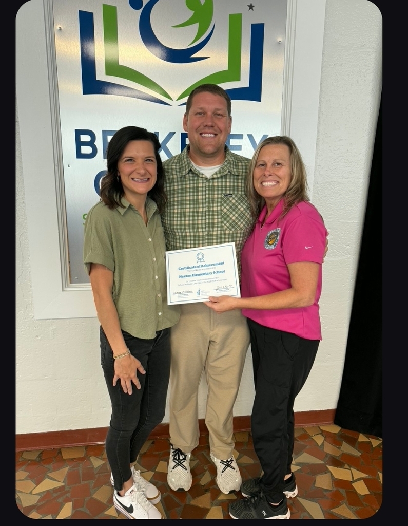 Three people stand before a sign. The man in the middle holds a certificate. The women are smiling.