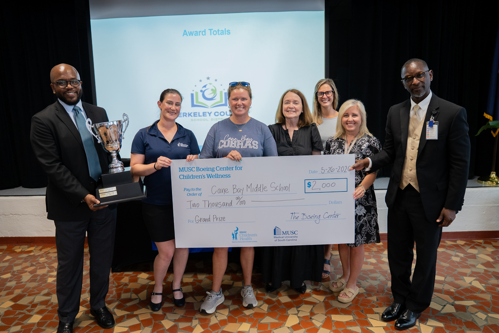 People pose for a photo with a check and trophy in a conference room. A man holds a trophy, and a woman holds a check.