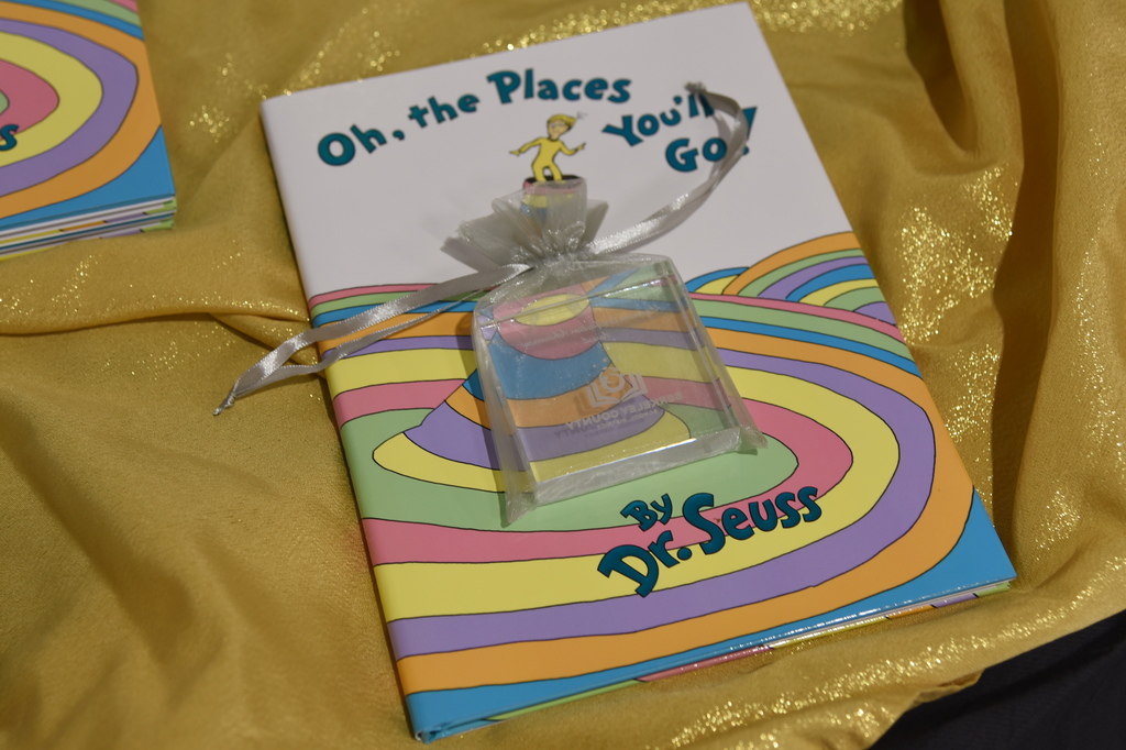 A book titled "Oh, the Places You'll Go!" by Dr. Seuss, with a colorful spiral design, featuring a small glass block.