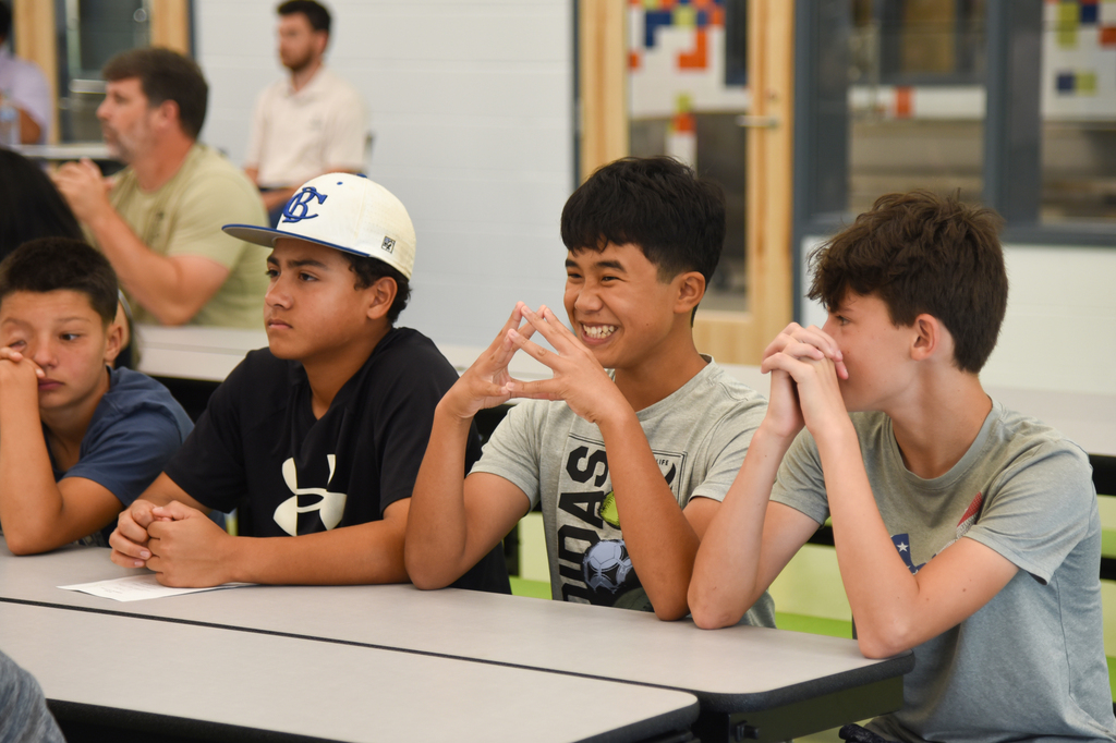Four boys in a classroom setting. Two are smiling and making a peace sign, another has hands on his chin, and one has his hands on a desk.