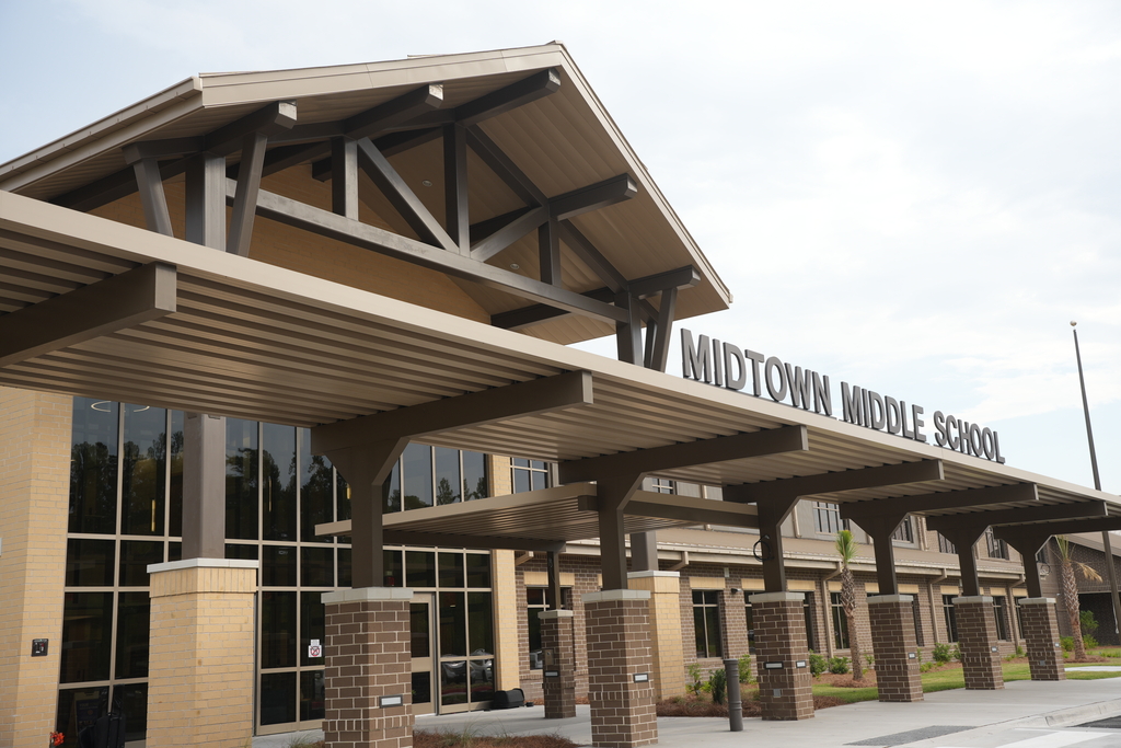 Entrance of Midtown Middle School building with a metal roof, glass windows, and a sign above the entrance.