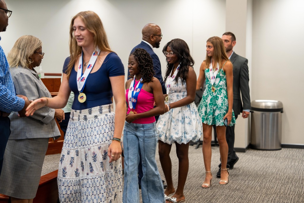 A group of people in formal wear, some with medals, standing in a conference room.