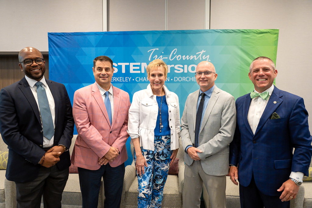 Five individuals in formal attire standing together in front of a banner with the words "Tri-Country OSTERIO".