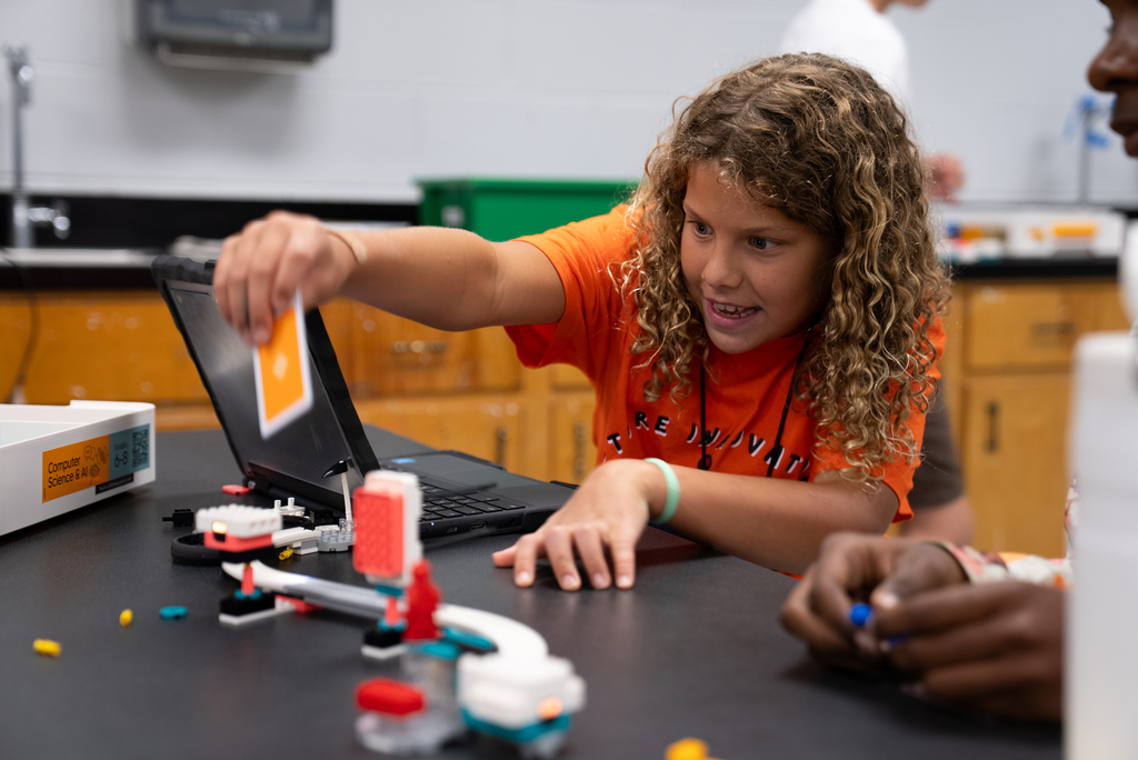 A student, with curly hair, uses a computer while another person works beside them on a project.