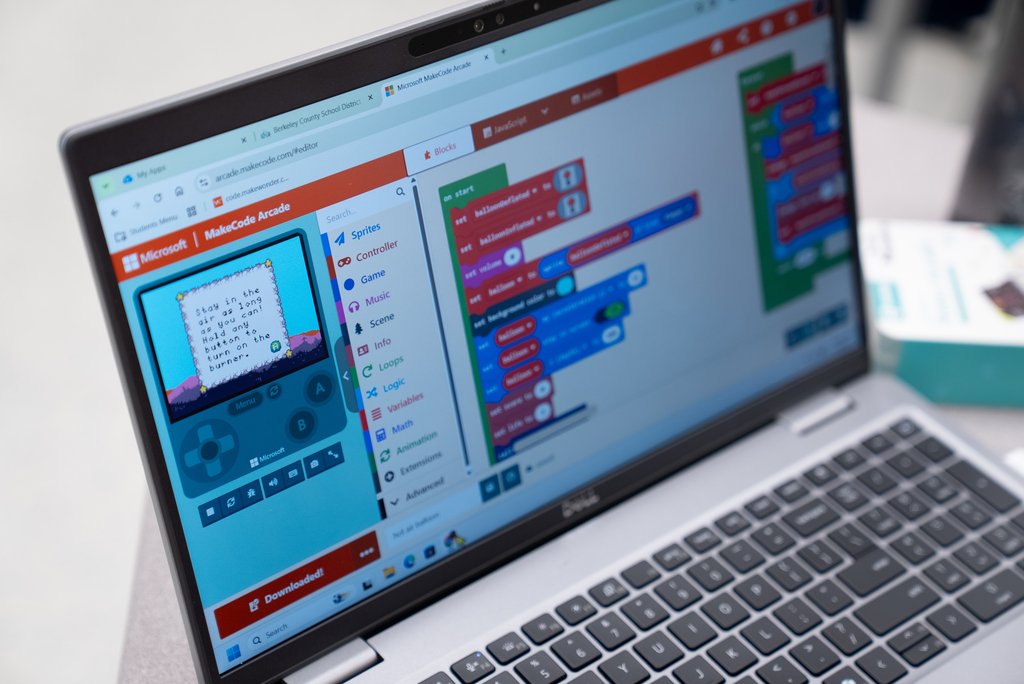 Laptop displaying a coding program with a game controller interface on screen. Keys on the keyboard are visible.