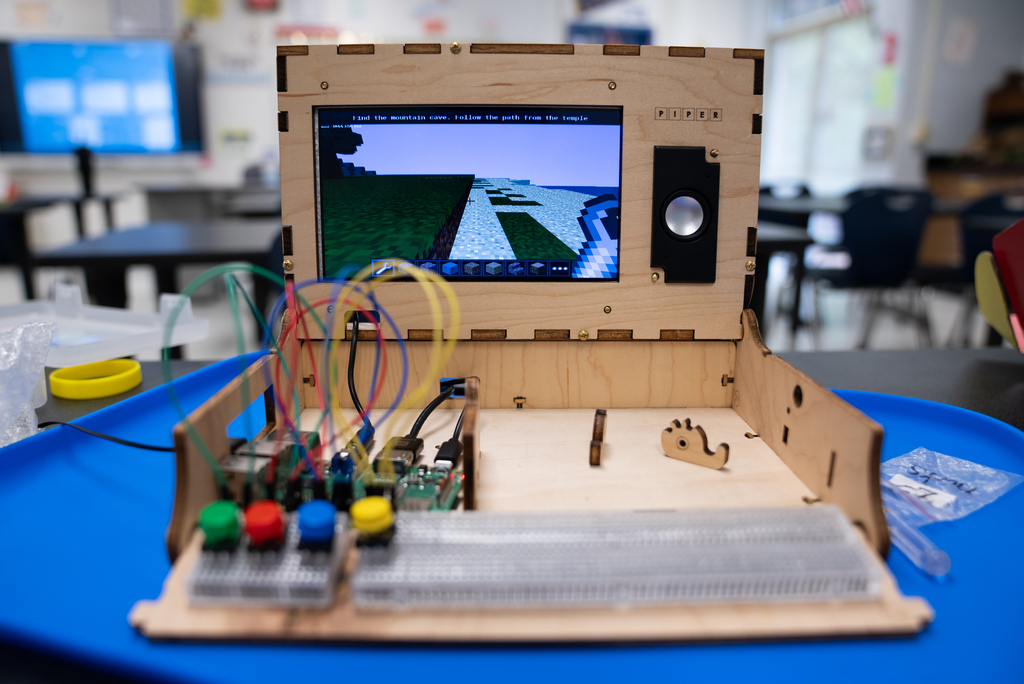 A wooden electronic device resembling a computer. It has a screen, buttons, and wires. On a blue table.