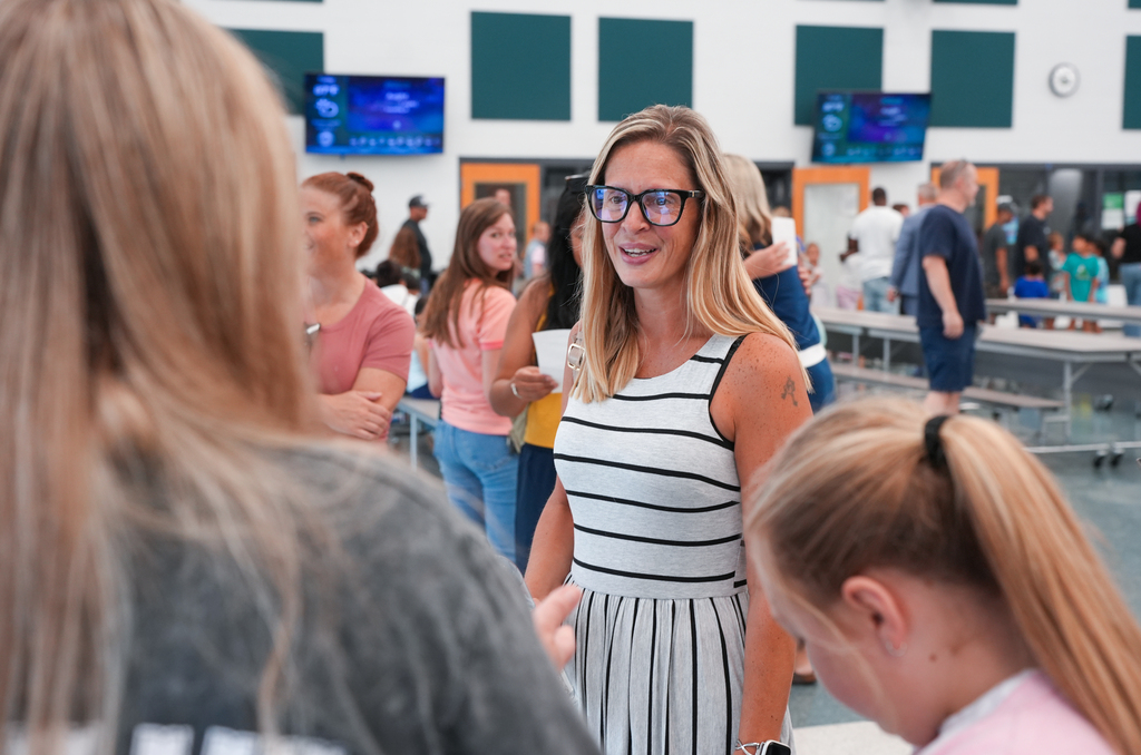 A woman in a black-and-white dress and glasses talks with a girl with a ponytail.