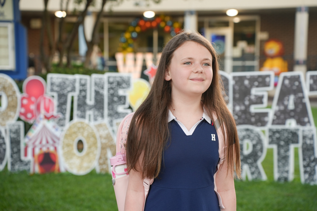 A young girl stands in front of a colorful, large sign 