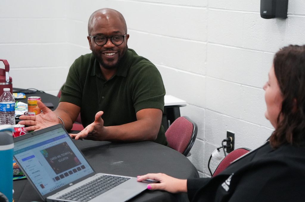 Man and woman seated at a table with a laptop. The man smiles and gestures with his hands.