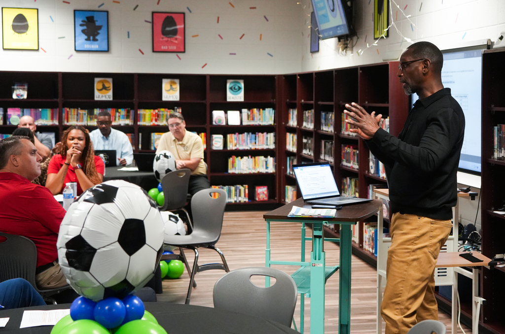 A man stands in a library with a soccer ball on a table in front of him.