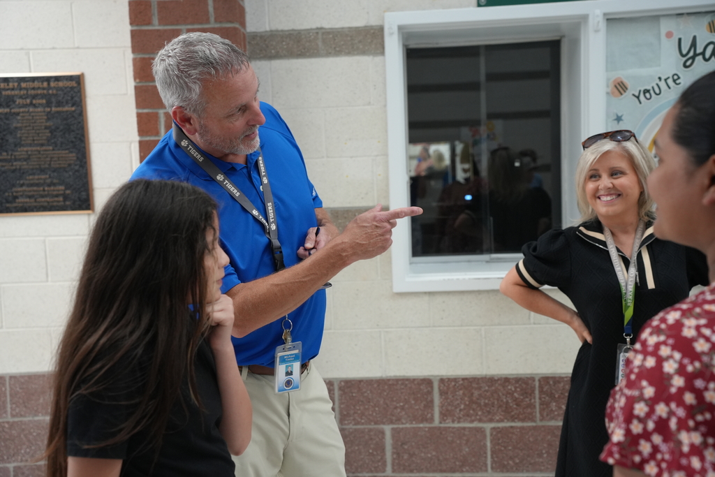 A man in a blue shirt points outside a window while two women and a girl listen.