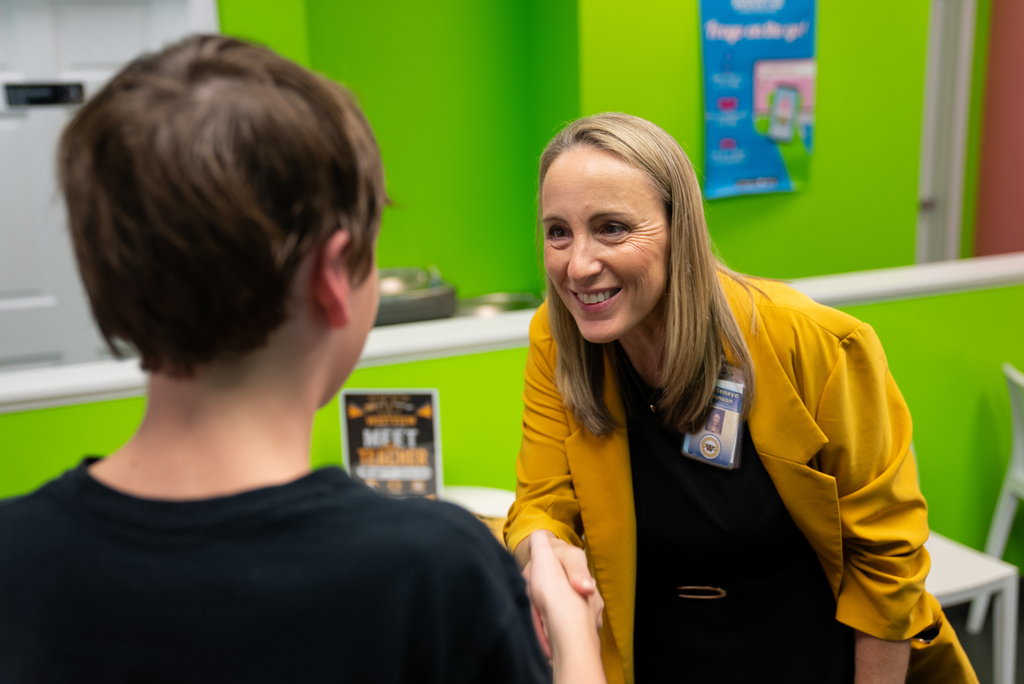 A woman in a yellow coat smiles while shaking hands with a boy in a black t-shirt.