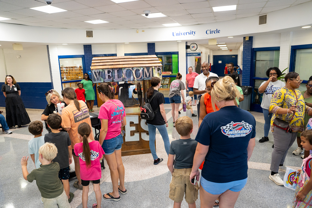 A group of adults and children in a hallway. One adult holds a sign that reads "Welcome".