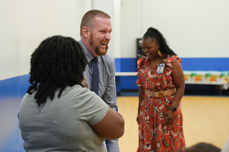 Three adults stand and talk in a room with a blue and white wall and a wooden floor.