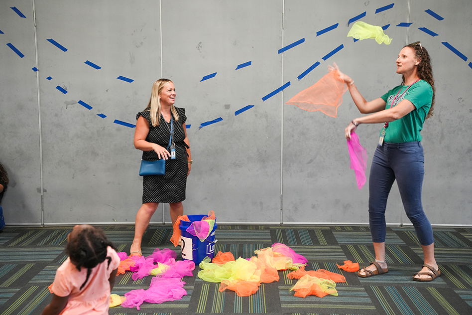 Two women and a child on a floor. One woman is tossing paper into the air.