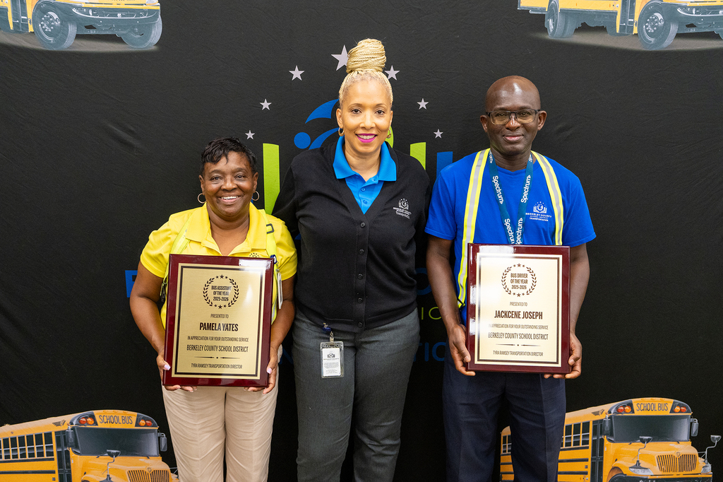 Three adults stand together, holding framed certificates. One holds a certificate with a blue cover, another with a yellow cover.