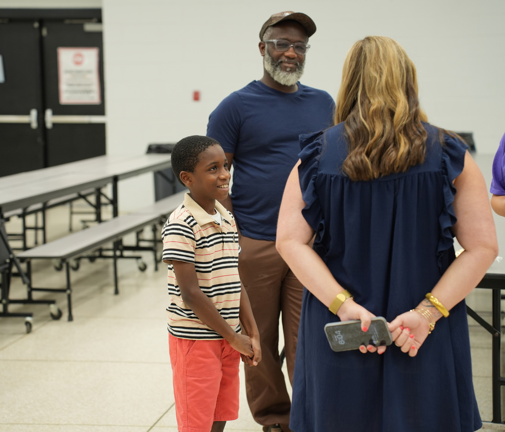 A family of three stands in a room with a white wall. A man and woman face a young boy.