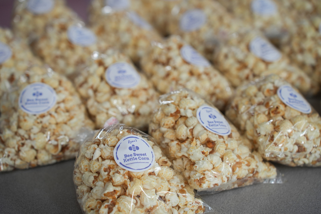Numerous bags of popcorn, each with a blue label reading "Best Sweet Saltine Corn." The popcorn has a golden-brown color and appears freshly popped.