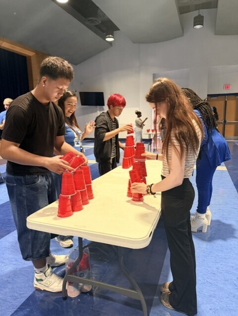 A group of people stand around a table filled with red cups, preparing to play a stacking game.
