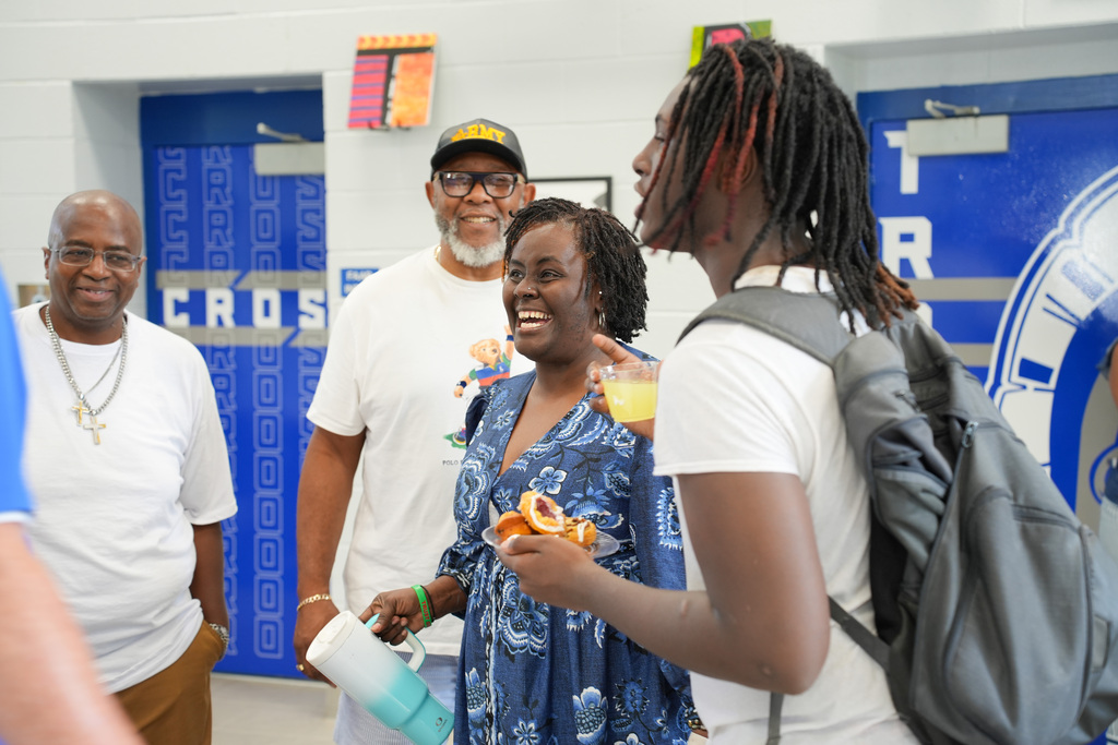 Five people in a hallway, one with a backpack, smiling and talking to each other.