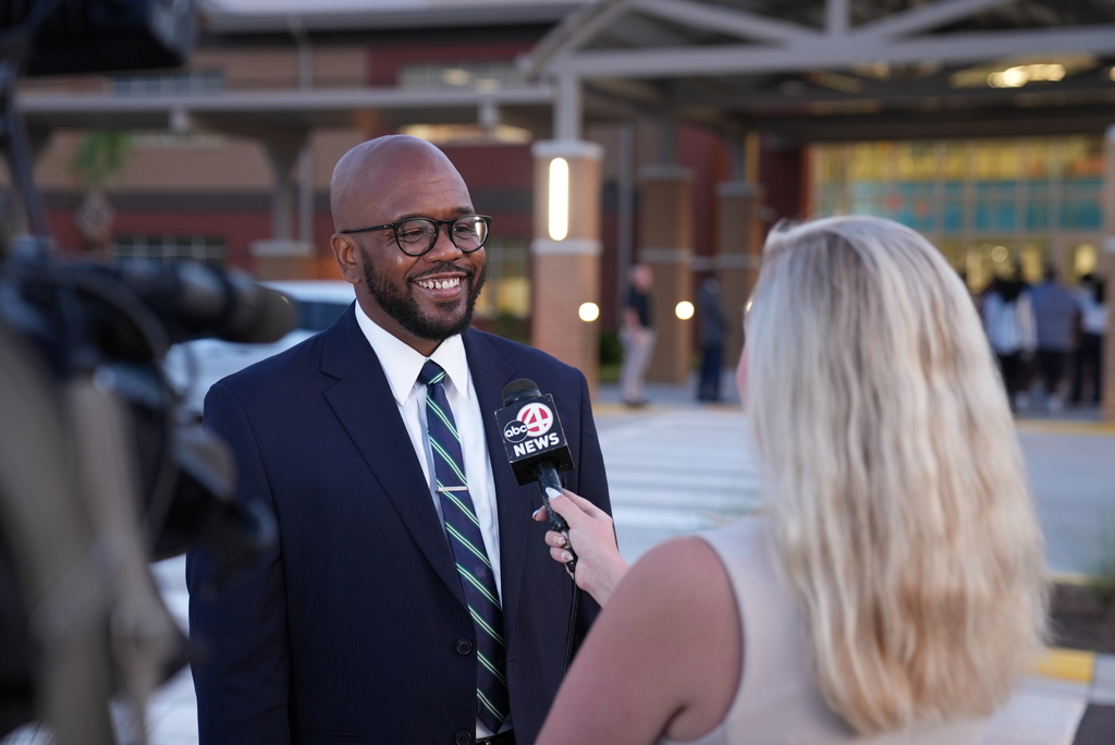 A man in a suit and tie is being interviewed by a woman with blonde hair, outdoors.