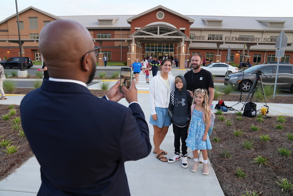 A man takes a photo of three children and two adults standing on a sidewalk in front of a building.