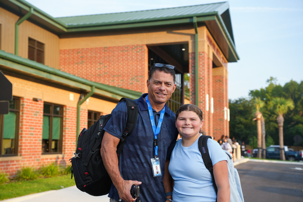 Person in blue shirt with backpack stands with another person in blue shirt and backpack in front of brick building.