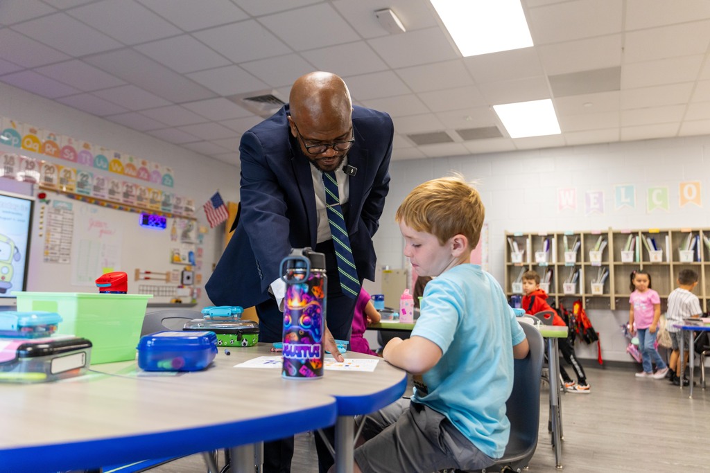 A man in a suit and tie bends over a desk while a young boy in a blue shirt sits there.