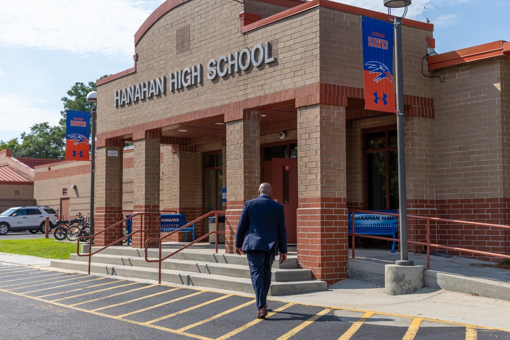 Person in a blue suit walks toward the entrance of Hanahan High School. The school has a red roof and brick walls.