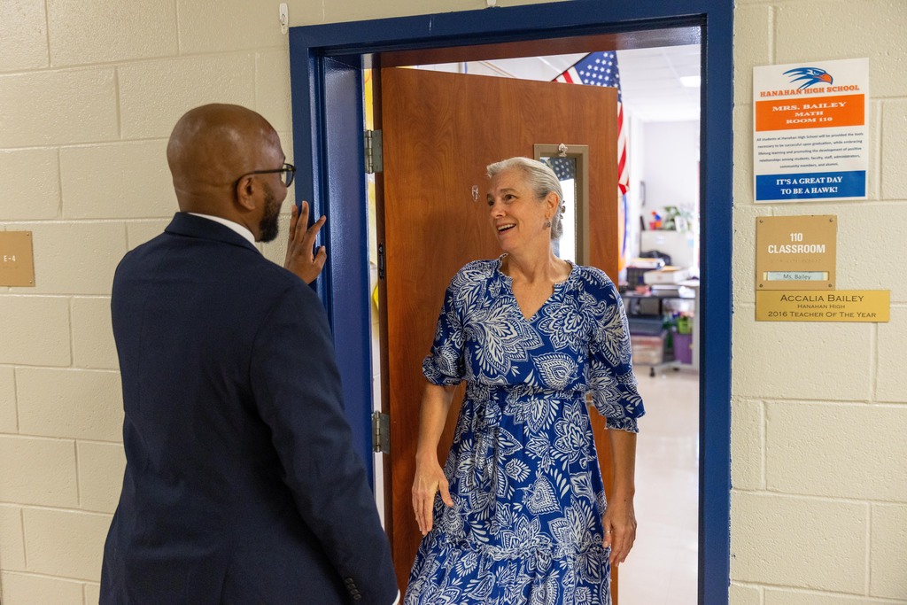 A man in a dark suit and a woman in a blue dress stand near an open door.